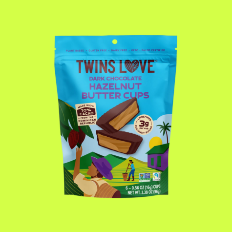 A package of Twins Love Dark Chocolate Hazelnut Butter Cups. Packaging includes an illustration of cocoa farmers in a tropical climate tending to their crop, and it also identifies the treat as plant-based, gluten-free, and dairy-free, as well as Paleo certified, and Non-GMO verified. The chocolate is 70% cacao which has all been sourced on Fairtrade terms from farms in the Dominican Republic.