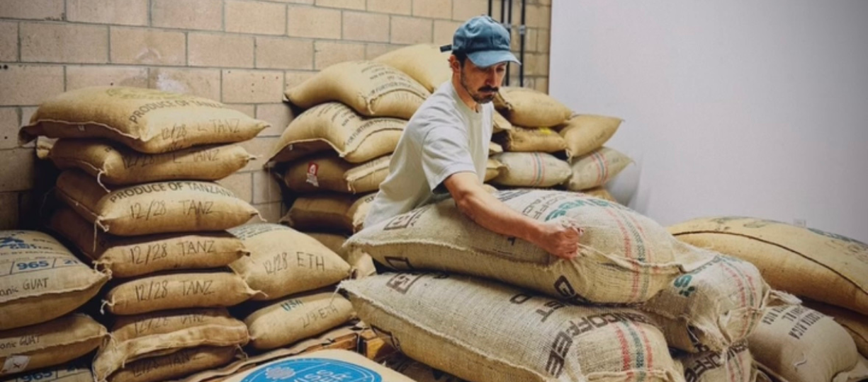 Ed Burga lifts a sack of coffee beans from a pile in a warehouse.