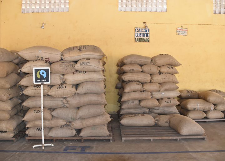 Bags of cocoa beans are stacked on a pallet. In front of them is a hand-drawn sign of the Fairtrade Mark.