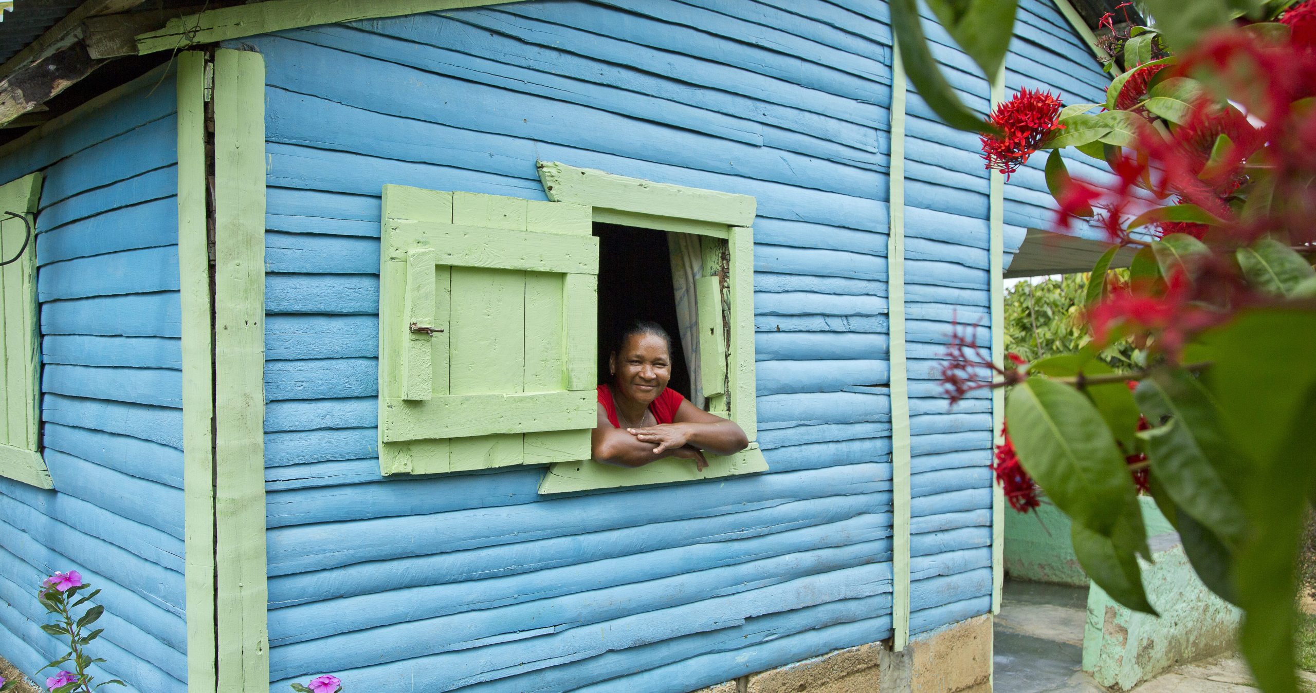 Carlixta Contreras Martínez looks out a window whose shudders are open and rests her arms against the window sill.