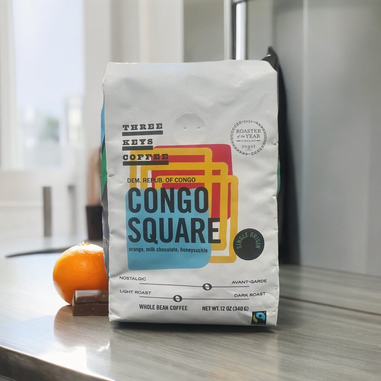 A bag of “Congo Square” roast from Three Keys Coffee which bears the Fairtrade Mark sites on a countertop next to a small orange and a square of chocolate.