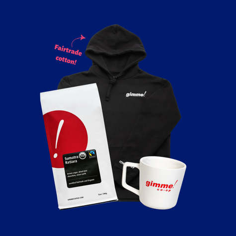 A bag of Gimme! Coffee's Sumatra Ketiara roast accompanied by a Fairtrade cotton sweatshirt that has Gimme's logo emblazoned on it, plus mug that has the logo for Gimme! Co-op on it.