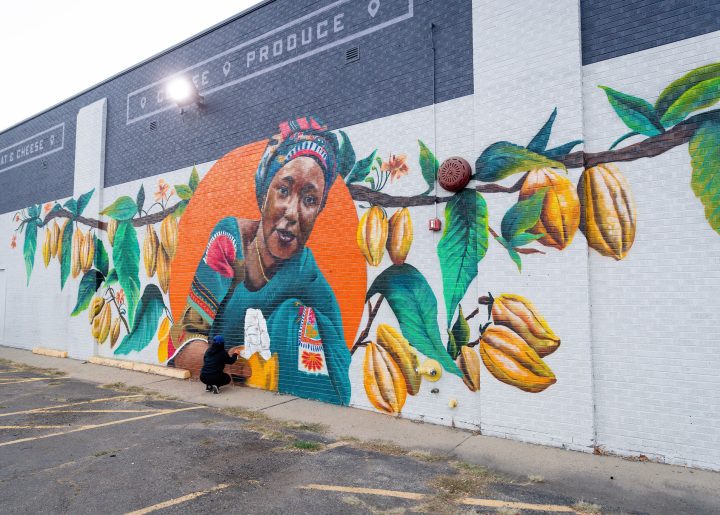 Artist Chelsea Lewinski crouches in front of her mural of Salamatu Katta to paint small details.