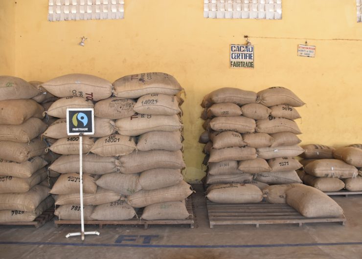 Bags of cocoa beans are stacked on a pallet. In front of them is a hand-drawn sign of the Fairtrade Mark.