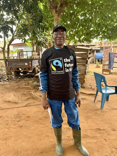 Ghanaian cocoa farmer Daniel Amponsah smiles to the camera as he stands in front of his home. He wears a Fairtrade t-shirt.