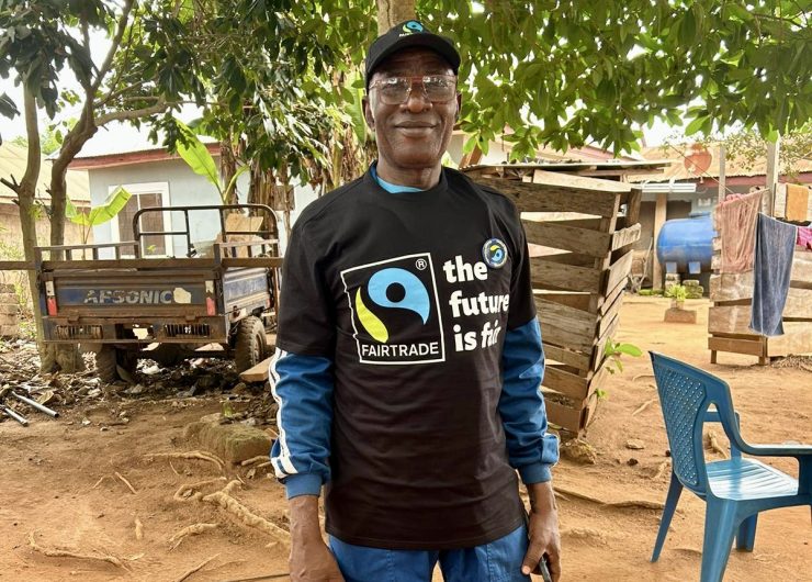 Ghanaian cocoa farmer Daniel Amponsah smiles to the camera as he stands in front of his home. He wears a Fairtrade t-shirt.