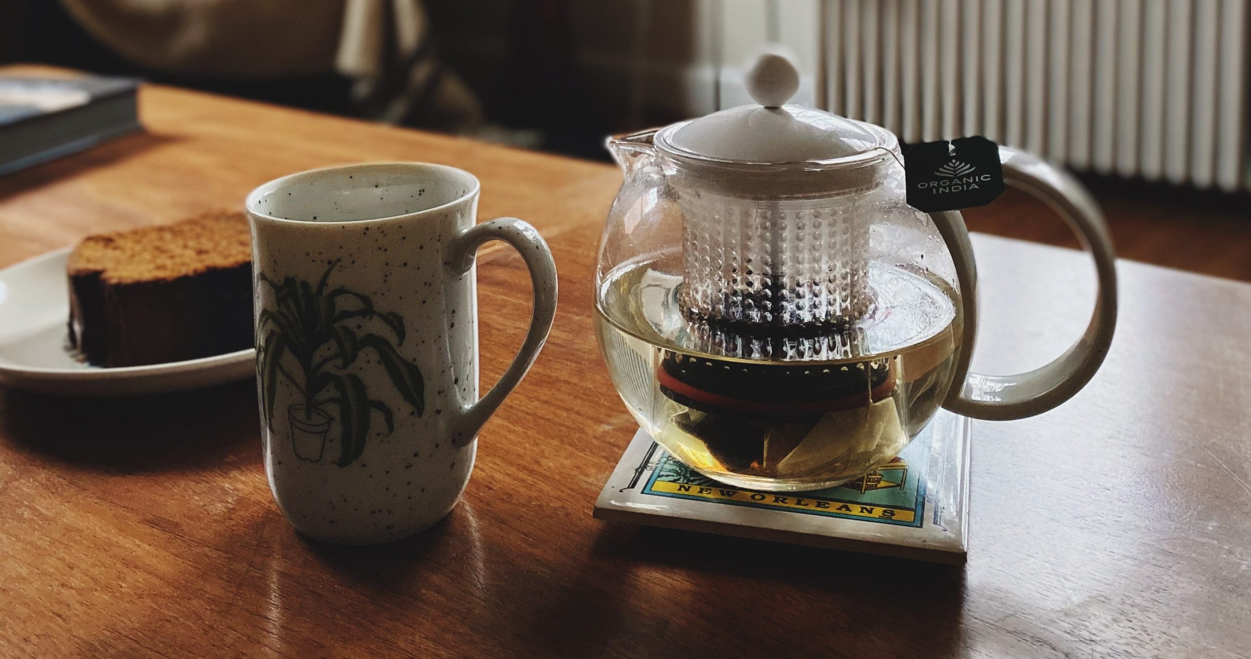 A cozy scene at home featuring a coffee table with a brewing pot of tea, an expectant mug, and a thick slice of pumpkin bread.