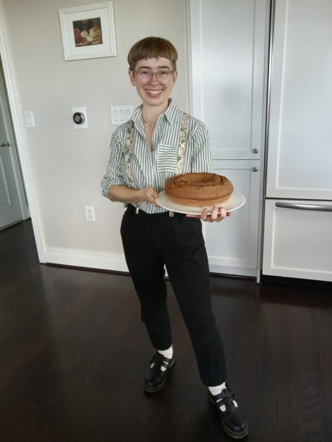 Caly stands in a kitchen and holds a pound cake on a white platter.