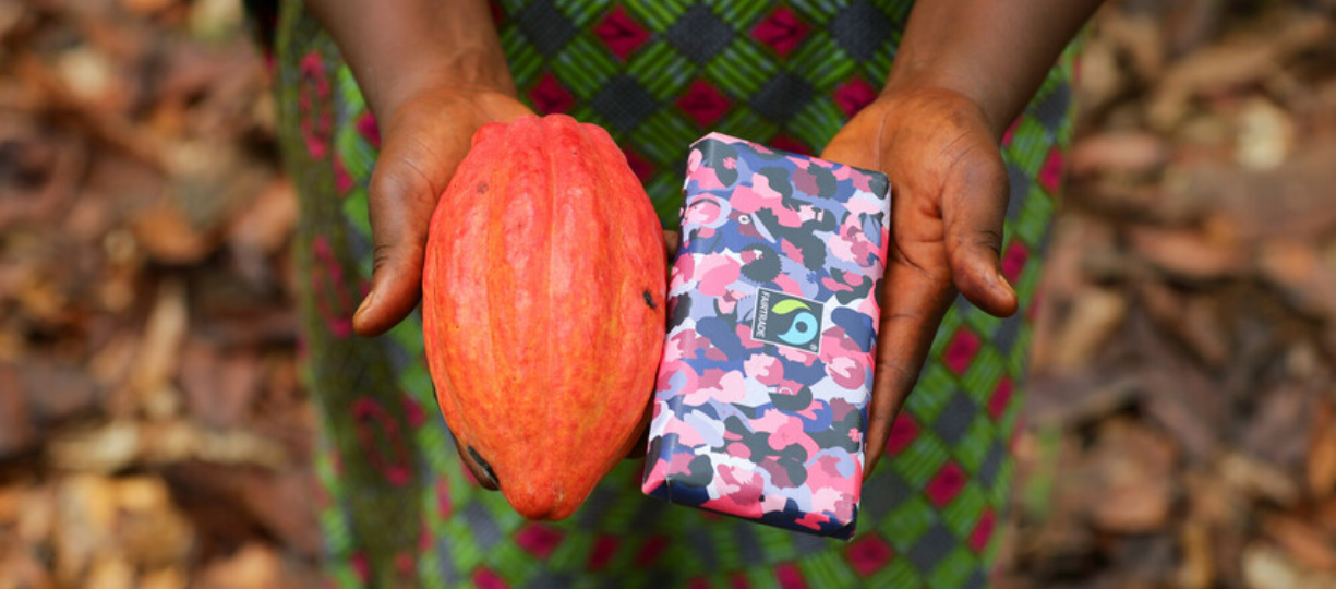 Dora Atiiga holds in her right hand a red cocoa pod and in her left hand a Fairtrade chocolate bar.